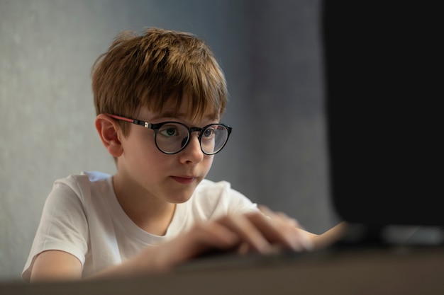 Niño de gafas juega con entusiasmo juegos de computadora. El muchacho adolescente está estudiando en línea. Preparándose para los exámenes.