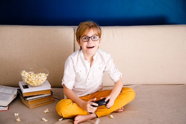 niño con gafas juega videojuegos sostiene un mando come palomitas de maíz en lugar de aprender lecciones