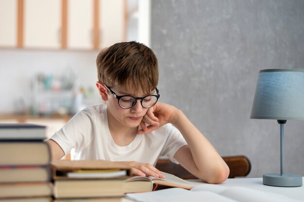 Niño con gafas lee libros mientras está sentado en la casa. El niño está haciendo la tarea. Educación en el hogar. La educación a distancia.