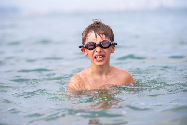 Un niño con gafas de natación nada en el mar.