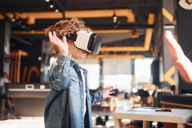 Niño con gafas de realidad virtual y ropa informal diviértase en la sala de juegos