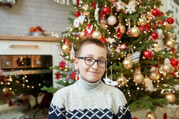 Niño con gafas sentado cerca del árbol de Navidad