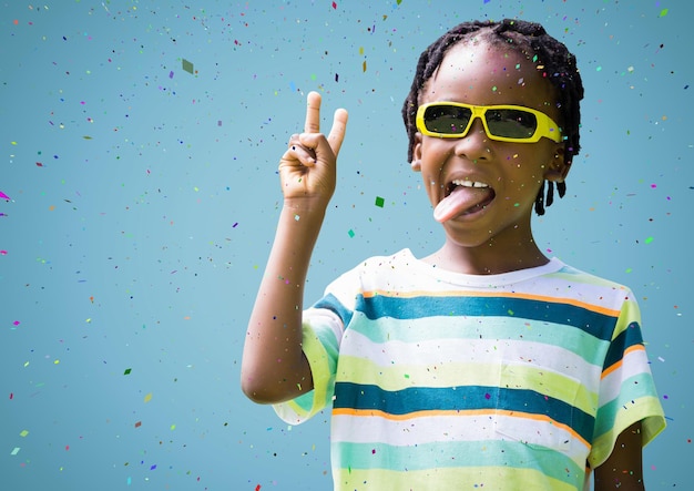 Niño con gafas de sol haciendo el signo de la paz contra el fondo azul y confeti