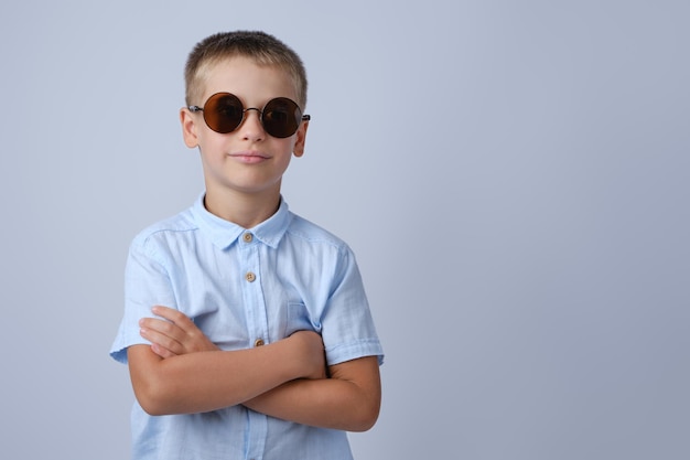 Un niño con gafas de sol redondas sobre un fondo gris con los brazos cruzados Lugar para el texto