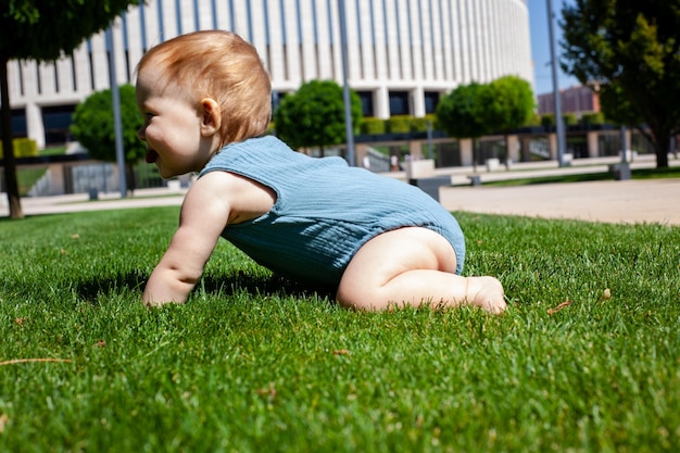 El niño gatea aprende a gatear sobre la hierba verde en el parque en verano