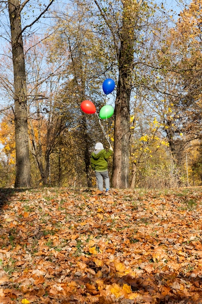 niño con un globo rojo verde y azul en la temporada de otoño