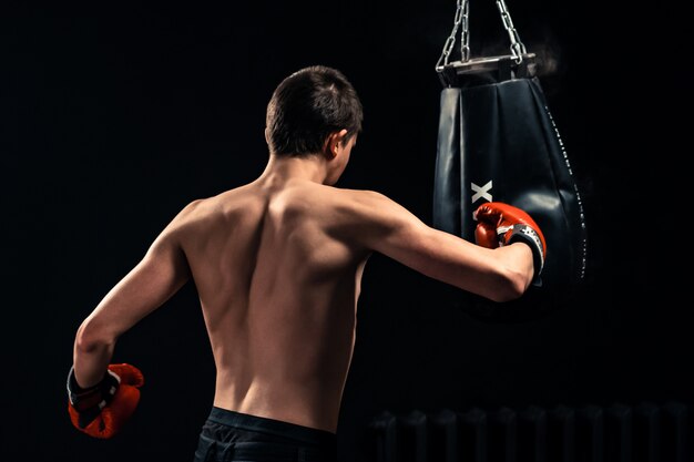 Niño golpeando el saco de boxeo sobre fondo oscuro