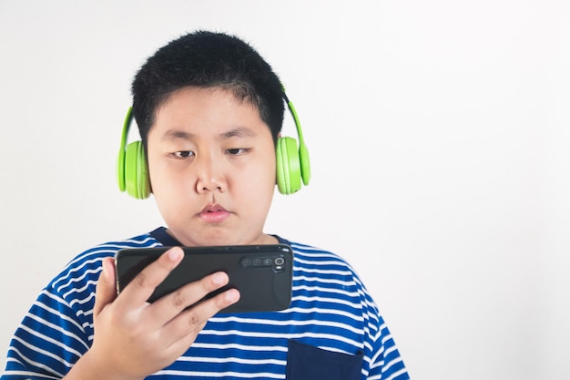 Niño gordo asiático usando auriculares y sosteniendo un teléfono inteligente Aprenda en línea a través de videollamadas con maestros. el concepto de educación a distancia utiliza tecnología moderna durante la epidemia de coronavirus