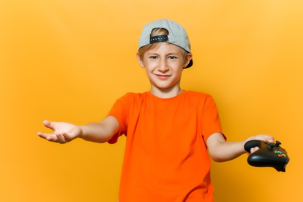 Un niño con una gorra y una camiseta naranja extiende sus manos en diferentes direcciones sostiene un mando en una mano