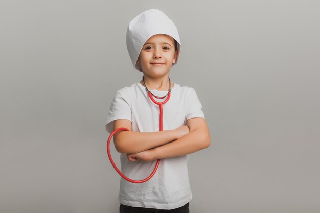 Niño con gorra de médico sostiene un estetoscopio sobre un fondo claro. pequeño doctor. foto de estudio de alta calidad