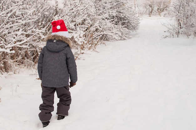 Un niño con una gorra roja de Navidad camina por un camino nevado