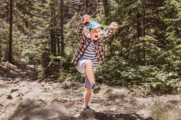 Niño con gorra verde representa a un dinosaurio malvado o un oso en el bosque en un camino de piedra