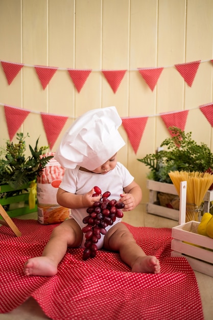 Un niño con un gorro de cocinero blanco sostiene uvas