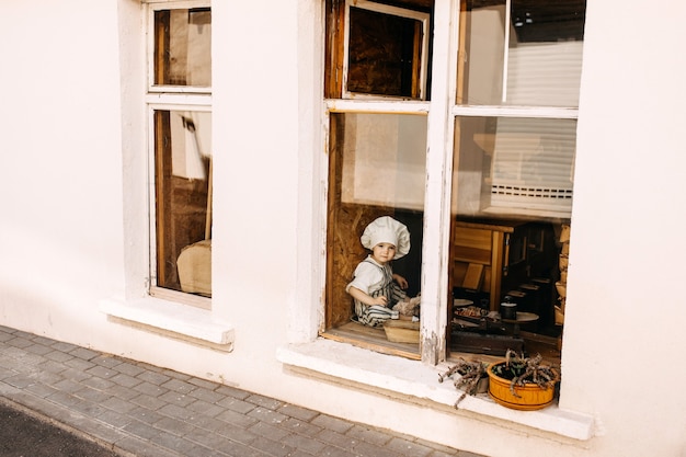 Foto niño con gorro de cocinero y delantal junto a la ventana