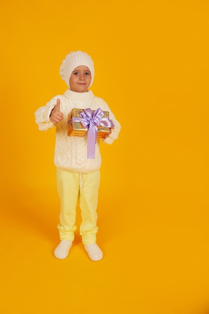 un niño con un gorro de invierno blanco con un suéter blanco tejido tiene una caja de regalo en sus manos