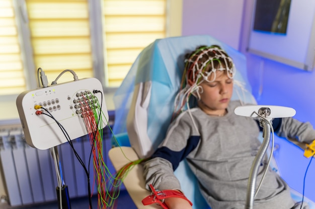 Niño con un gorro médico especial durante la electroencefalografía junto al monitor con lecturas.