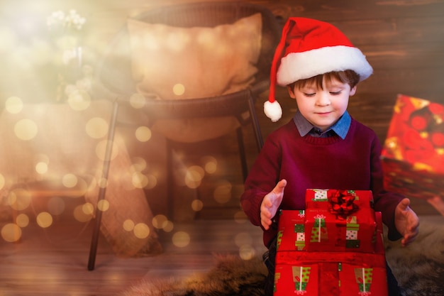 Niño con gorro de Papá Noel abriendo regalos