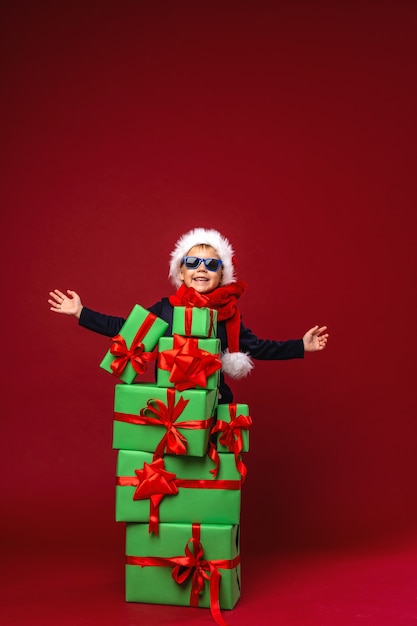 Un niño con un gorro de Papá Noel está detrás de cajas de regalo