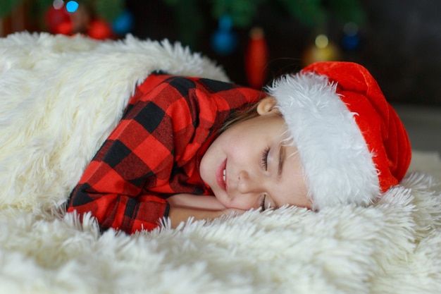 Un niño con un gorro de Papá Noel está durmiendo año nuevo.