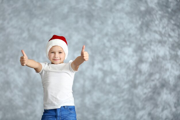 Niño con gorro de Papá Noel jugando sobre fondo gris