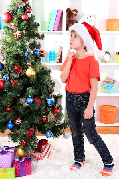 Niño con gorro de Papá Noel sueña cerca del árbol de Navidad