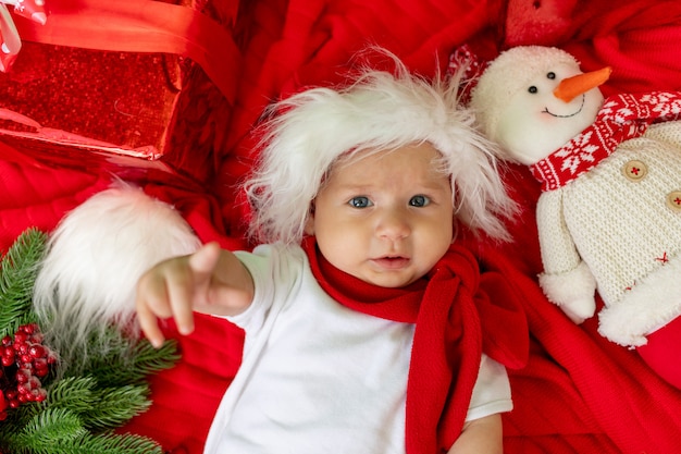 Un niño con un gorro de Papá Noel yace en rojo