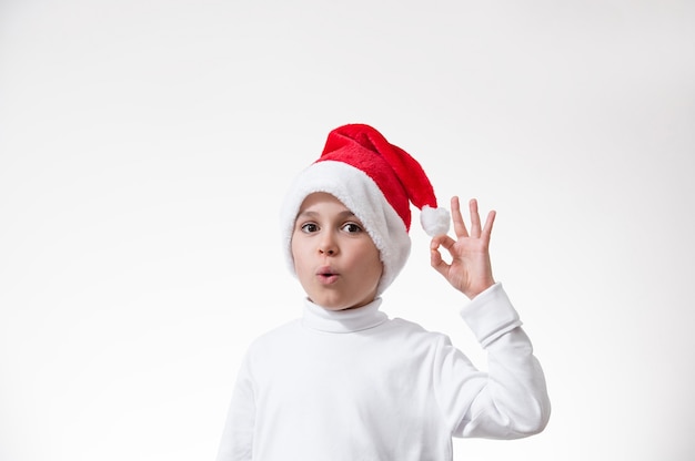 El niño con un gorro rojo de Papá Noel muestra un gesto de "ok". Concepto de navidad.