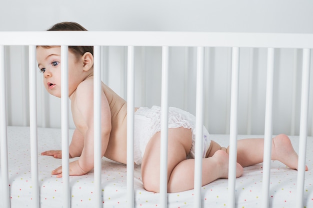 Niño gracioso acostado en la cama del bebé con expresión de cara de sorpresa