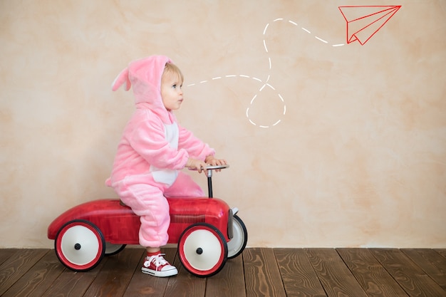 Niño gracioso con conejito de Pascua. Niño montando coche de juguete en casa.