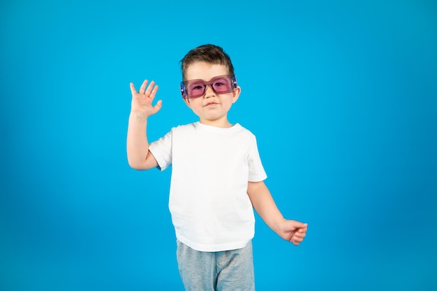 Niño gracioso con gafas violetas saludando a la cámara Fondo azul con espacio de copia Foto de alta calidad