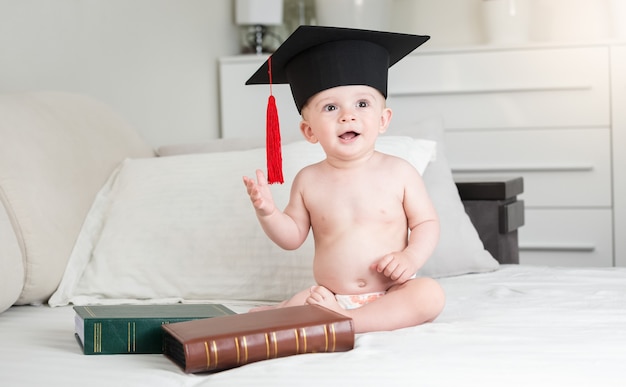 Niño gracioso en pañales con gorro de graduación negro