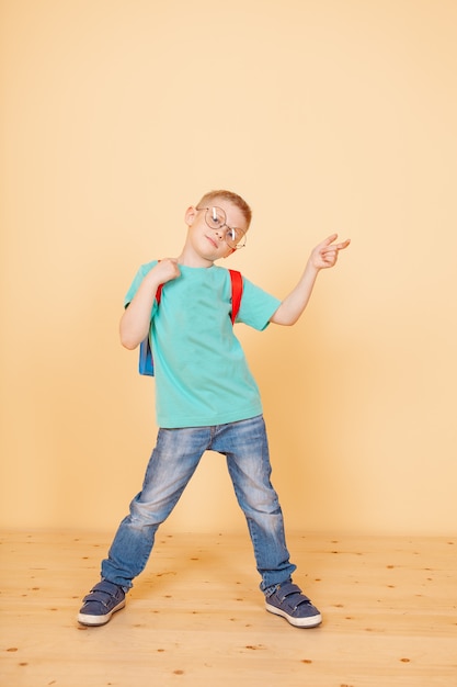 Niño gracioso de pie con gafas, mochila. Sorprendente. Aislado en el amarillo.