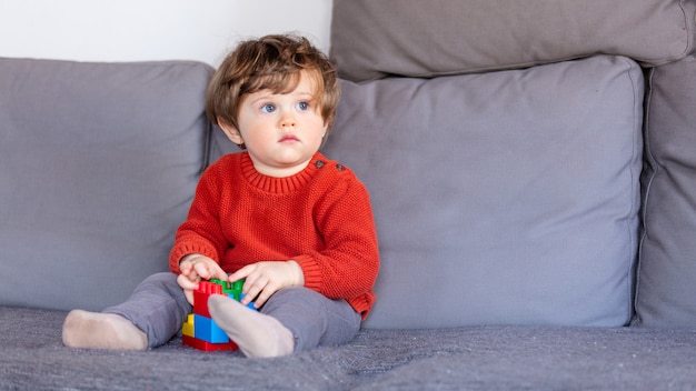 Niño gracioso que se sienta en el sofá en suéter rojo