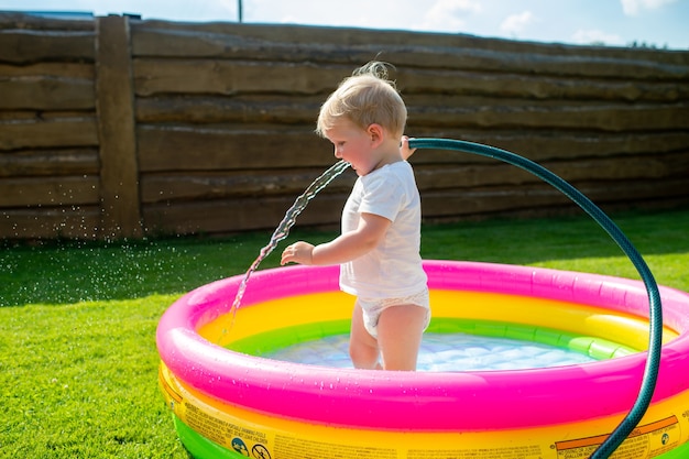 Un niño gracioso recogiendo agua en la piscina infantil.