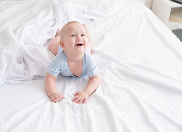 Niño gracioso sonriendo y acostado en una ropa de cama blanca en casa.