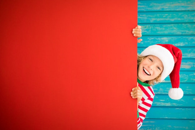 niño gracioso sosteniendo pancarta de cartón niño en blanco jugando en casa vacaciones de navidad