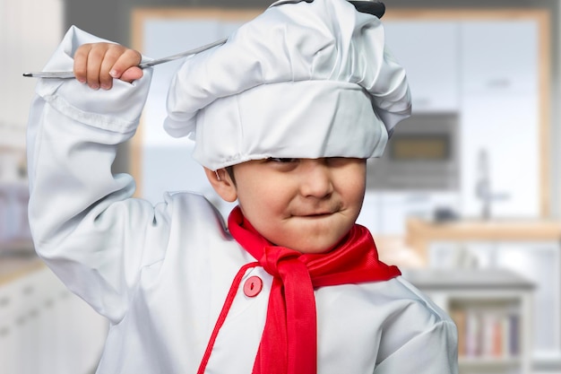 niño gracioso vestido de cocinero con una sartén golpeando la cabeza