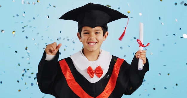 Foto niño graduado y celebración con confeti y baile feliz en el estudio sobre fondo azul para la educación desarrollo del niño y éxito con expresión emocionada diploma o certificado de logro