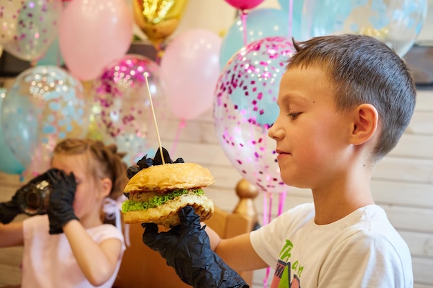 El niño guapo comiendo hamburguesas con guantes de goma negros