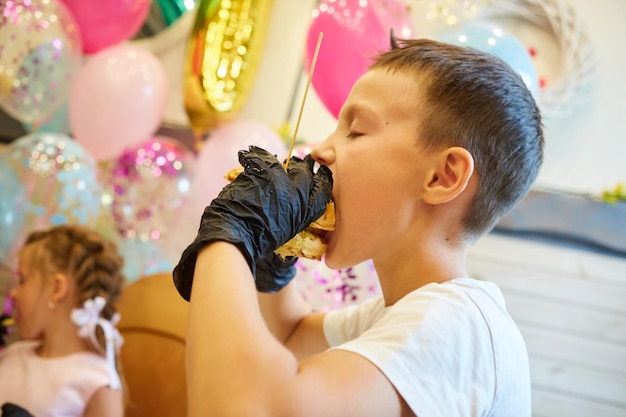 El niño guapo comiendo hamburguesas con guantes de goma negros