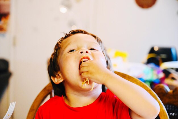 Foto un niño guapo y hambriento comiendo fideos mientras está sentado en casa.