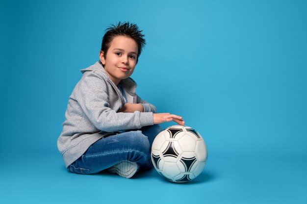 Niño guapo sentado cerca de un balón de fútbol