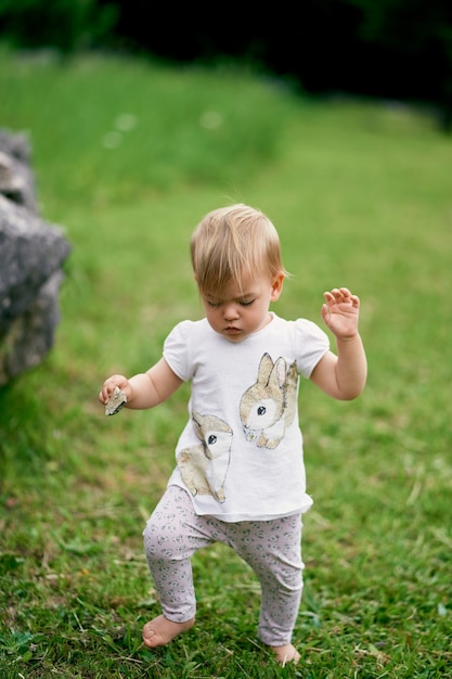 Niño con un guijarro en la mano camina por un prado verde