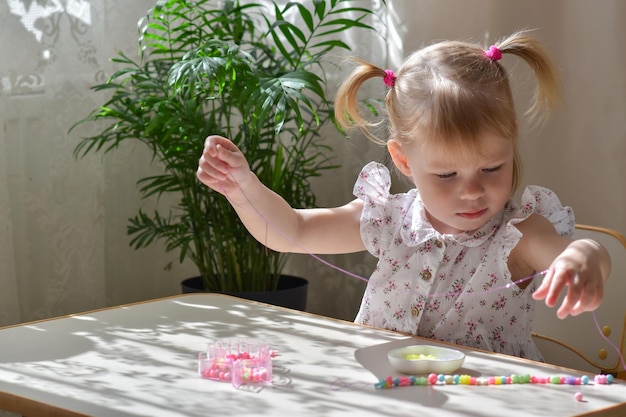 Un niño hace joyas con cuentas en la ventana de la mesa de la habitación.