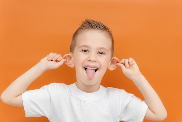 Un niño hace una mueca sobre un fondo naranja, un niño alegre caucásico muestra su lengua y tira hacia atrás