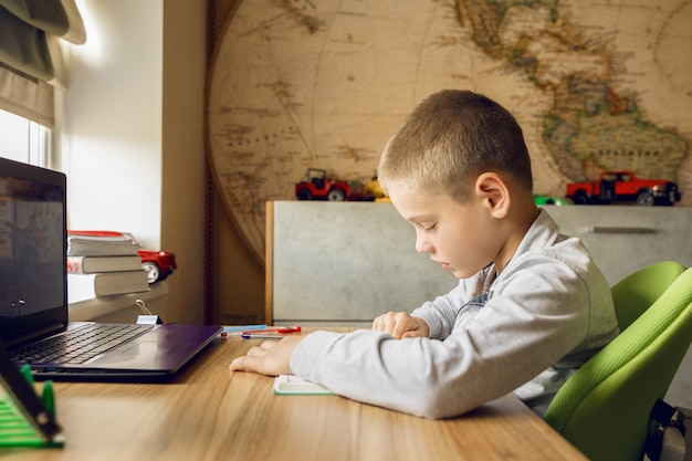 Un niño hace su tarea mientras aprende en línea.Un chico pasa el dedo por una línea en un libro.