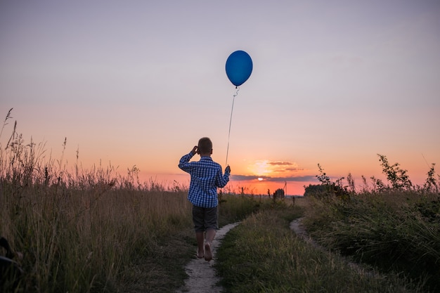 Niño hace sus sueños al aire libre con globo Correr por el campo Hermosa libertad de tarjeta de verano