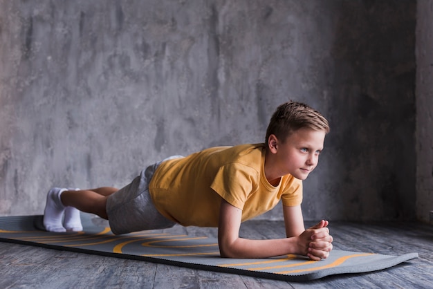 Foto niño haciendo ejercicio en la colchoneta frente a un muro de hormigón