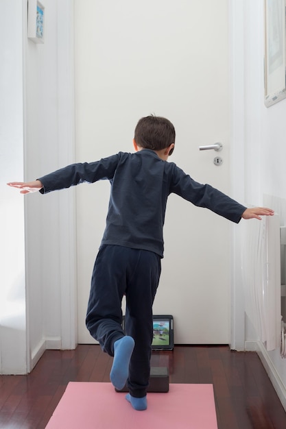 Niño haciendo ejercicios de gimnasia con una tableta en casa