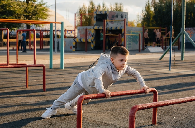 Un niño haciendo flexiones en el patio de recreo durante la puesta de sol. Deportes, estilo de vida saludable.